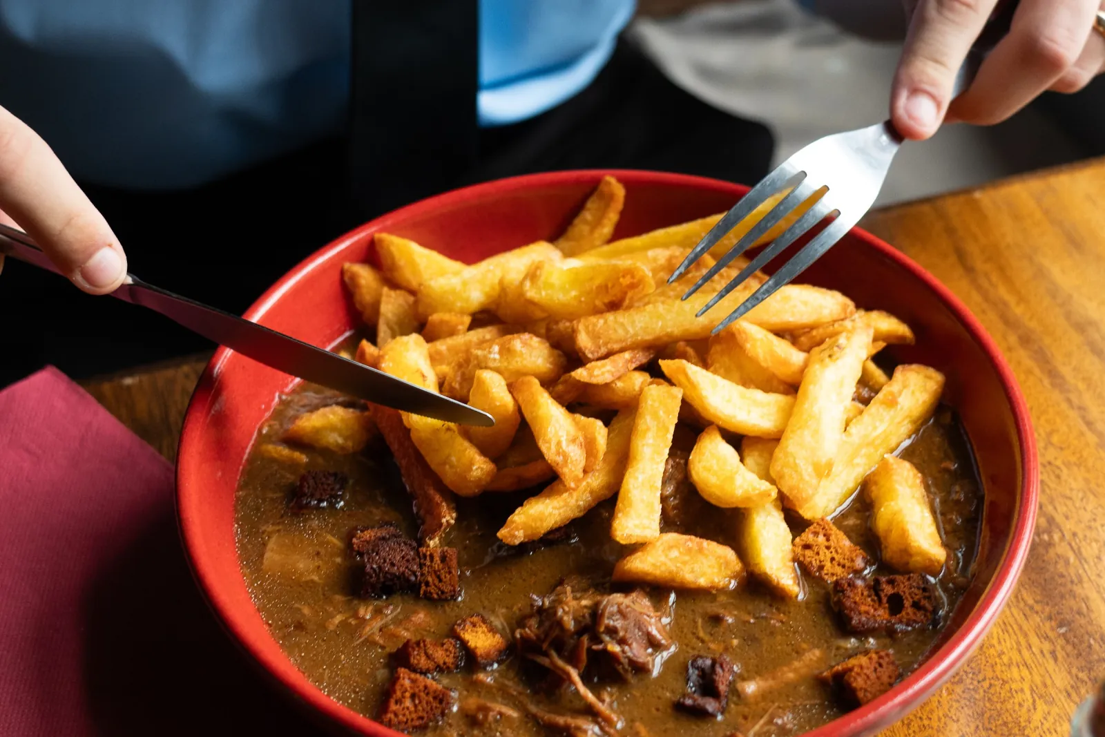 Une carbonade flamande et ses frites, dans un plat rouge, entre les mains d'un serveur.