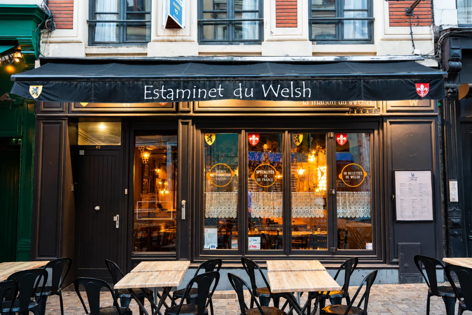 La devanture de l'Estaminet du Welsh, rue de Gand, store noir, vitrines éclairées et terrasse dressée sur les pavés.